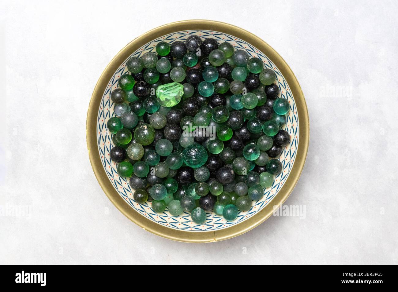 Vecchie sfere di marmo di vetro in una ciotola di plastica, isolate su bianco. Una pila nostalgica di classici giocattoli per bambini degli anni '1990. Vista dall'alto. Foto Stock