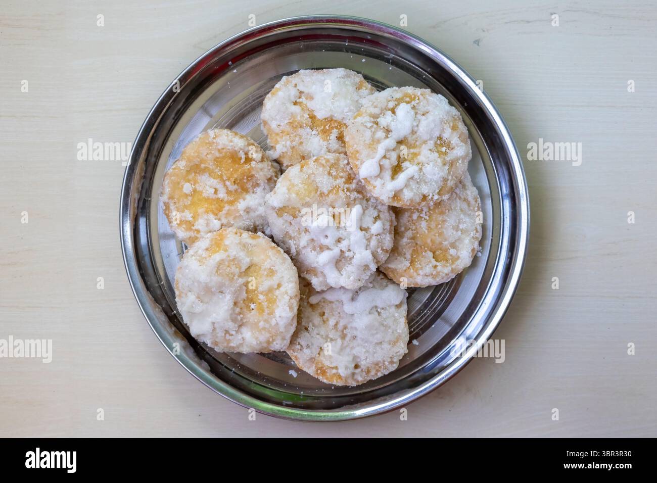 Deliziosa pasticceria rotonda Khaja o Khajuri su un piatto di acciaio, sfondo di legno. Questo dolce fritto in profondità, impregnato di sciroppo di zucchero e conosciuto come Gaja, è un populila Foto Stock