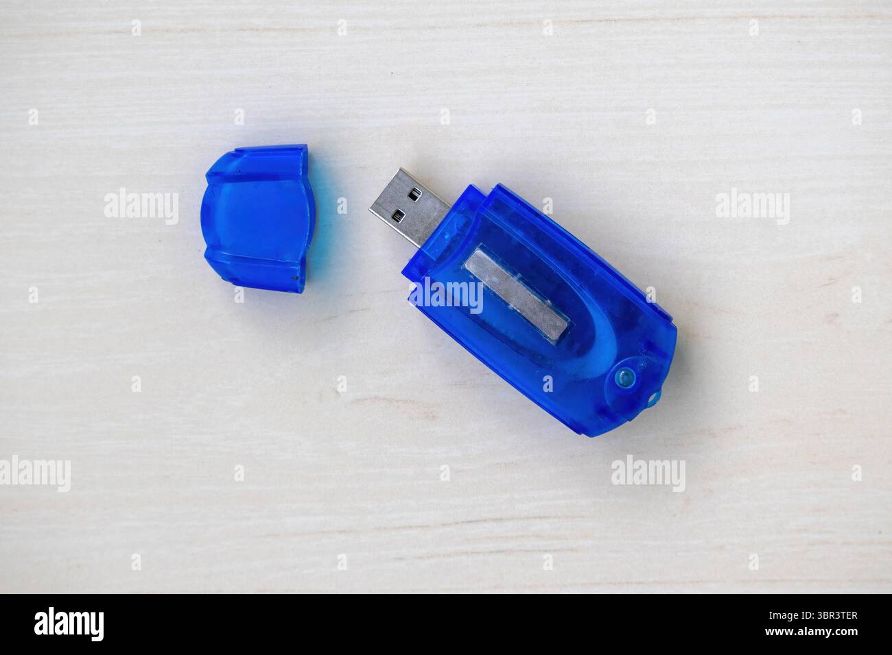Lettore di schede di memoria blu su legno chiaro. Il tappo si trova accanto ad esso. Vista dall'alto, primo piano dettagliato. Accessorio tecnologico essenziale per il trasferimento dei dati e l'archiviazione digitale Foto Stock