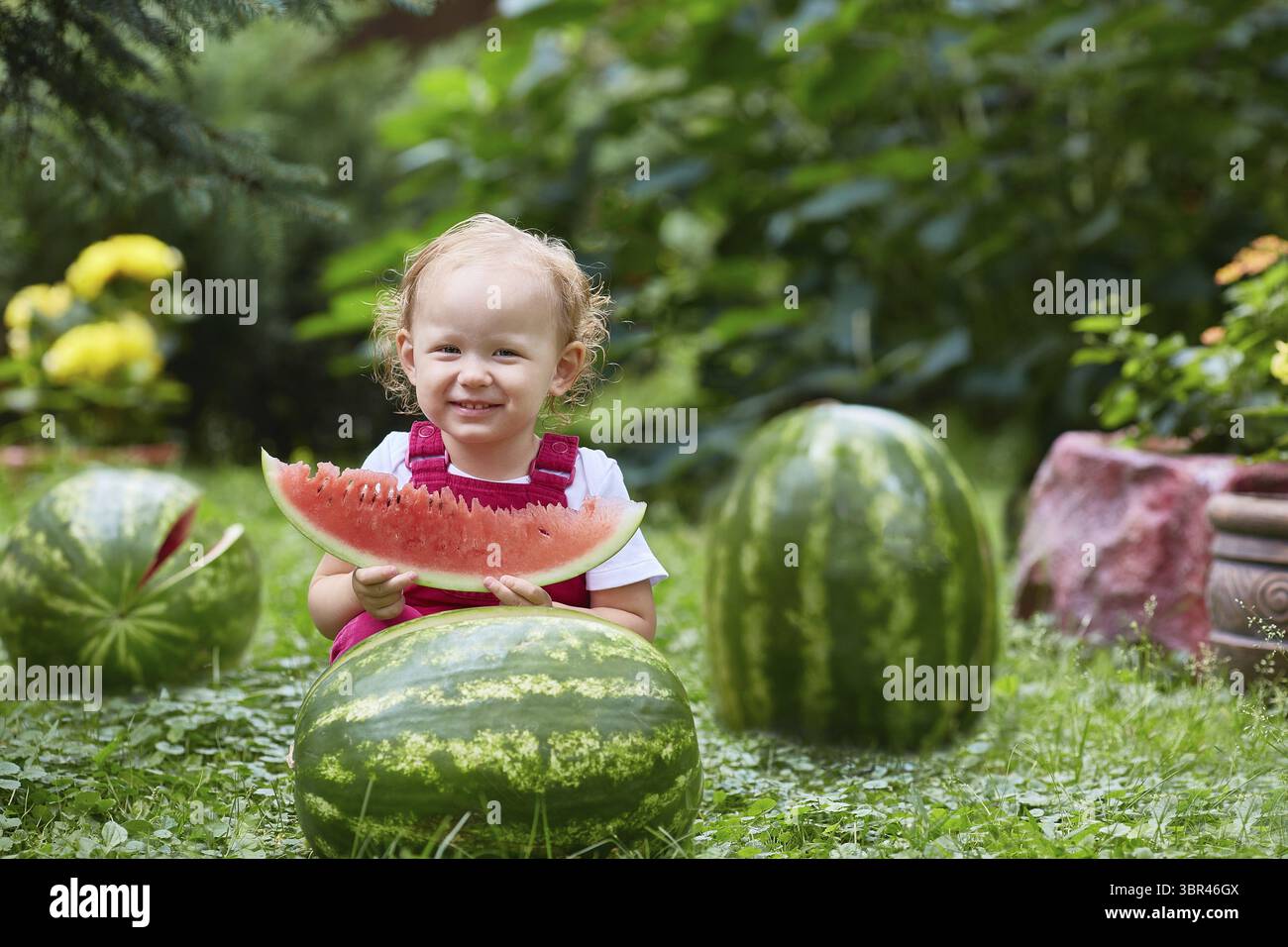 Bambino sorridente che mangia anguria in un prato con fiori in un giorno d'estate Foto Stock