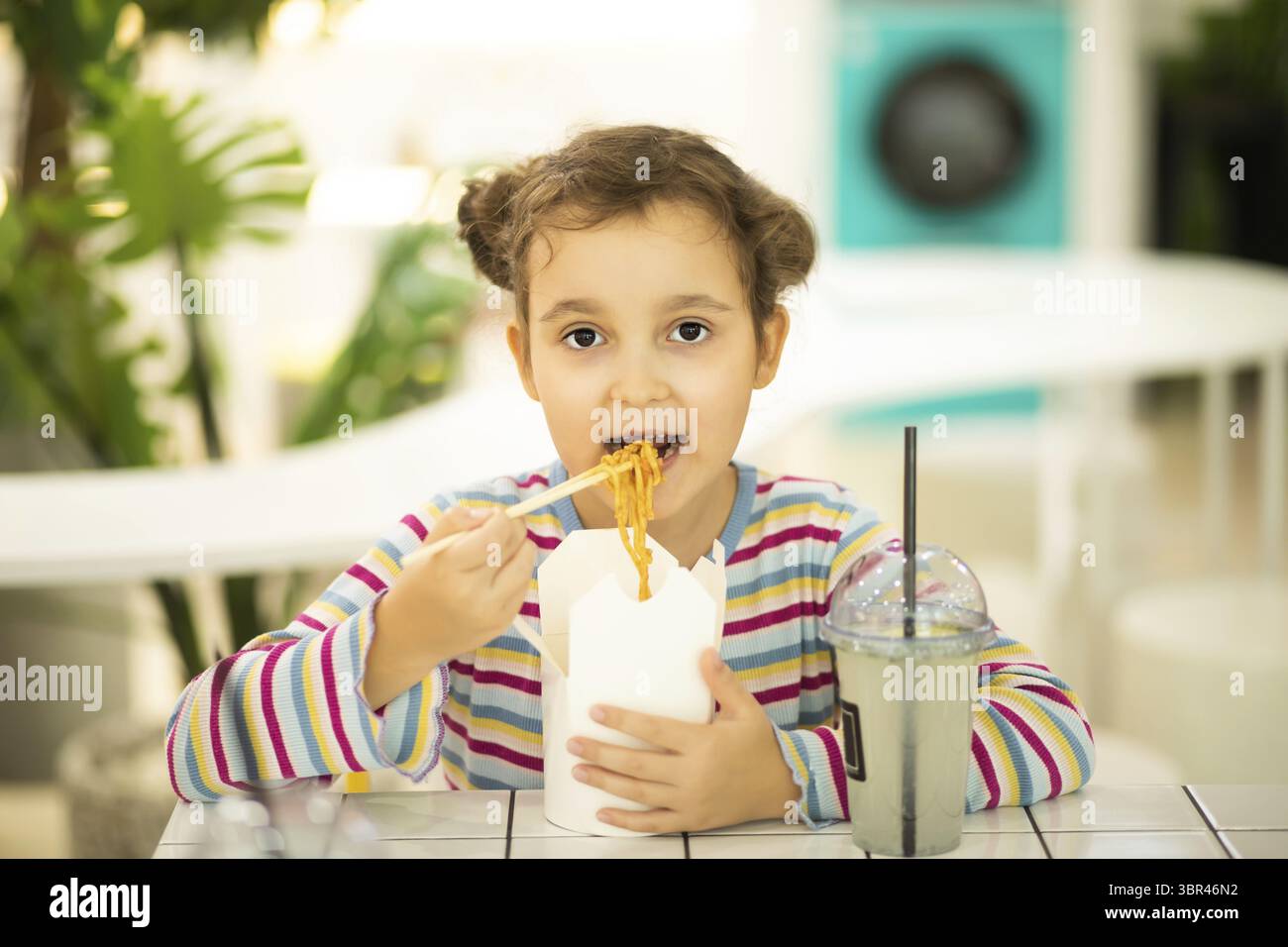Bambina che mangia ramen spaghetti wok con bacchette nel food Court. Ora di pranzo Foto Stock