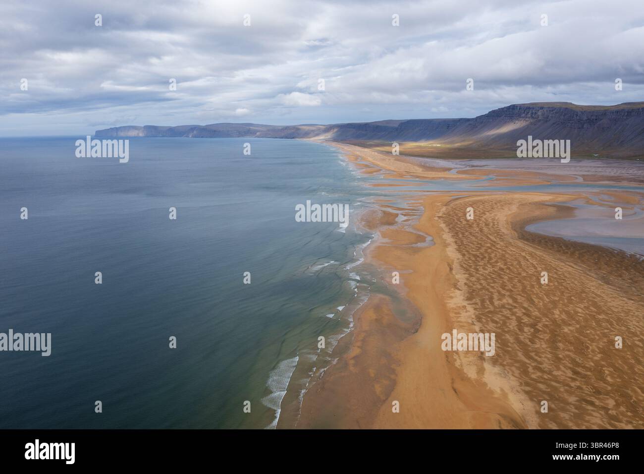Vista aerea della costa frastagliata dove le sabbie dorate incontrano il mare blu sotto un vasto cielo, Westfjords, Islanda. Foto Stock