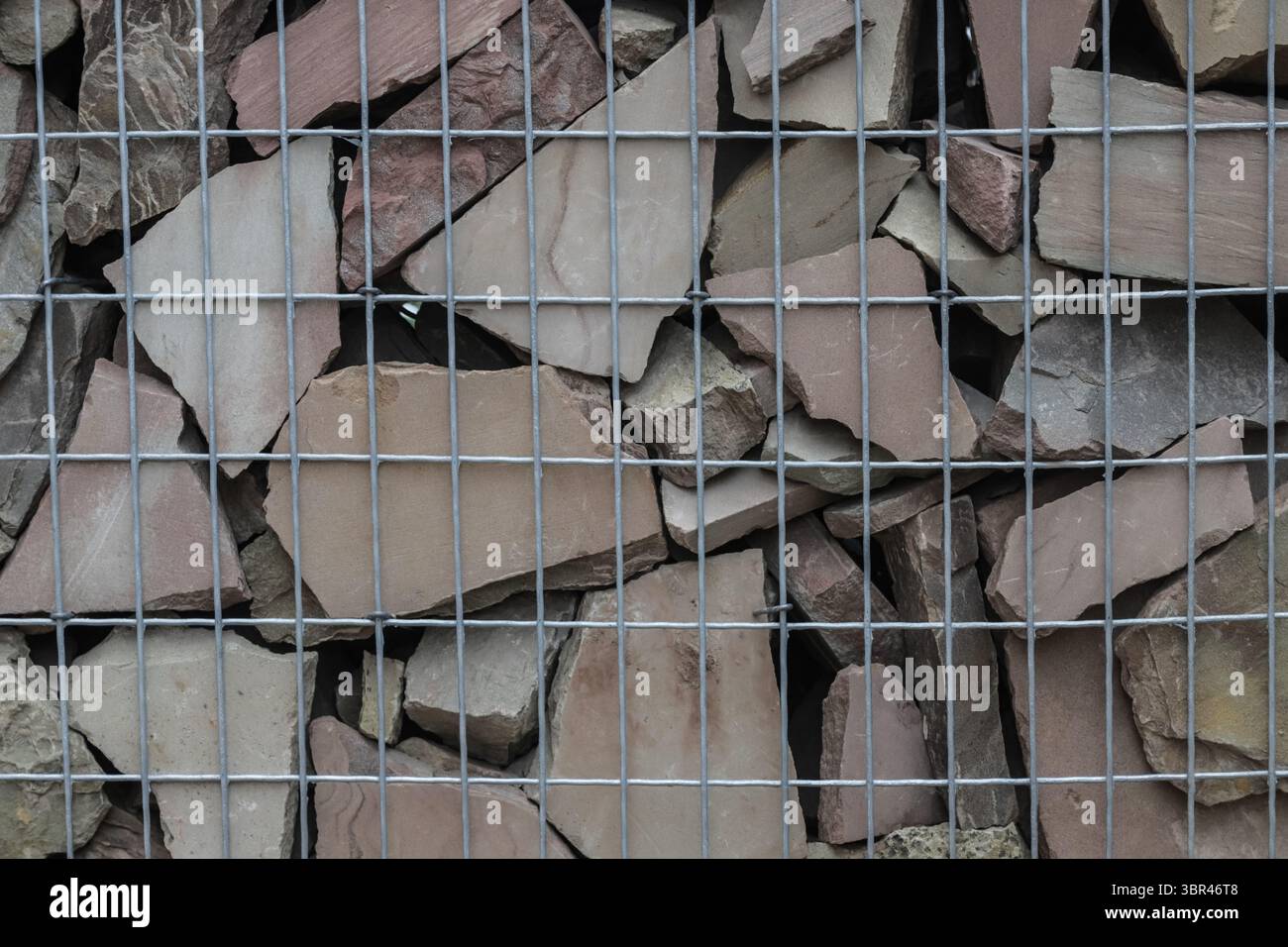 I frammenti di pietra robusti sono disposti con cura all'interno di una griglia metallica, per mostrare una pratica applicazione nell'edilizia o nell'architettura paesaggistica. Foto Stock