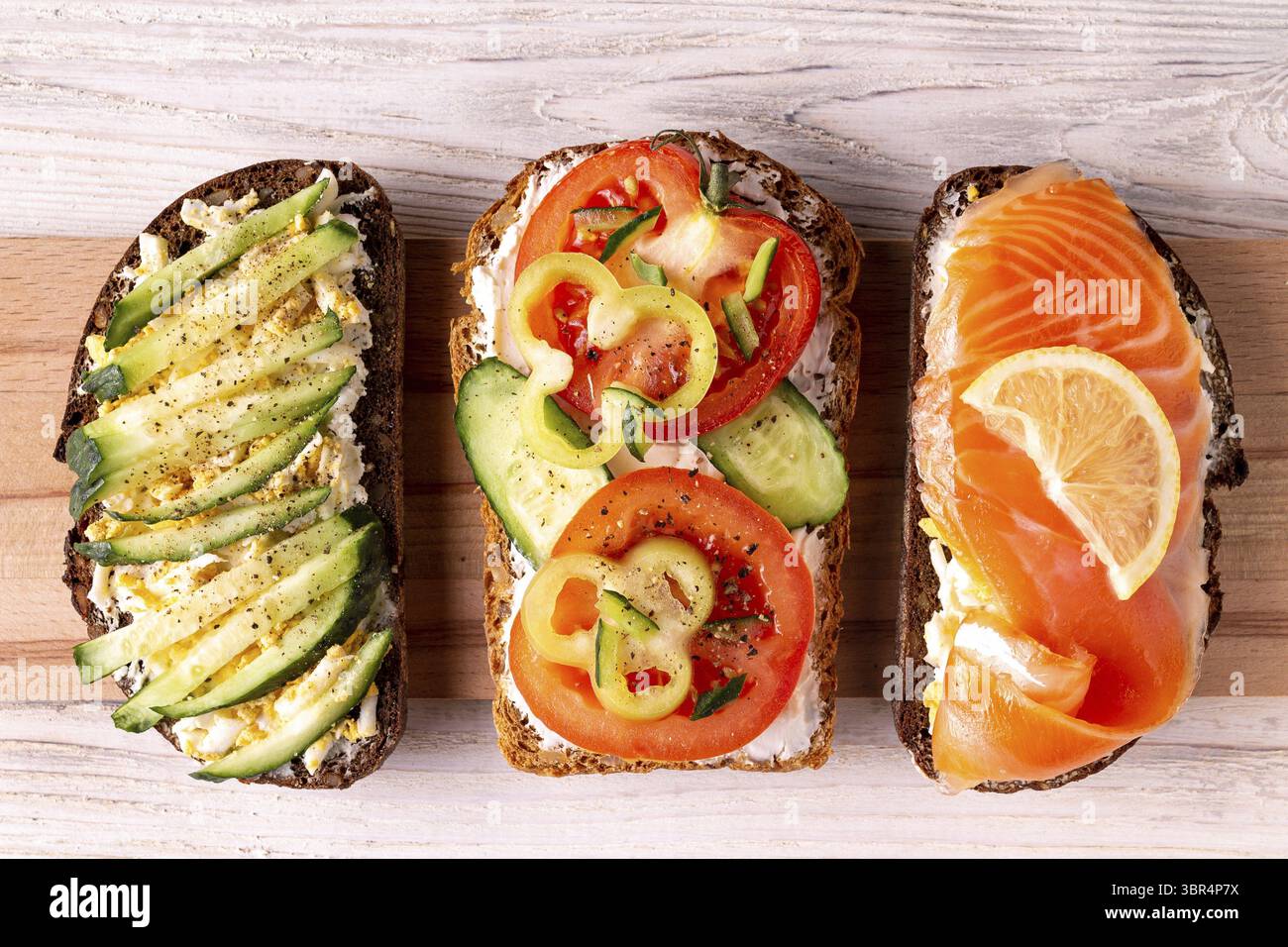 Panini con formaggio, trota salata, pomodoro, cetriolo su fondo bianco in legno Foto Stock