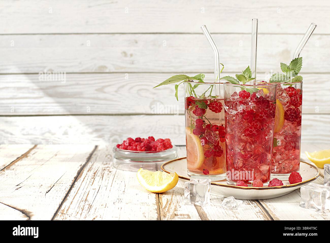 Natura morta moderna con succo di frutti di bosco, lamponi, ribes rosso, menta e arance su un tavolo da cucina soleggiato. Dieta disintossicante minima, vitamina d estiva Foto Stock