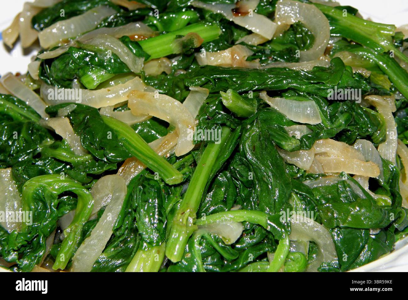 Spinaci freschi saltati con cipolla, una festa per il tratto digestivo e, nutrizionalmente Foto Stock