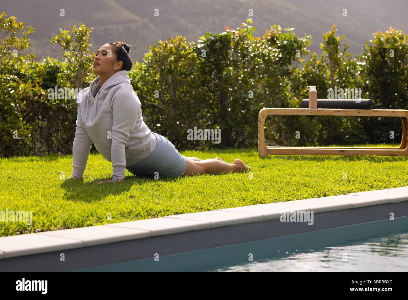 Donna asiatica che pratica yoga backbend nel cortile accanto alla piscina accanto alla panchina con rullo in schiuma, spazio copia Foto Stock