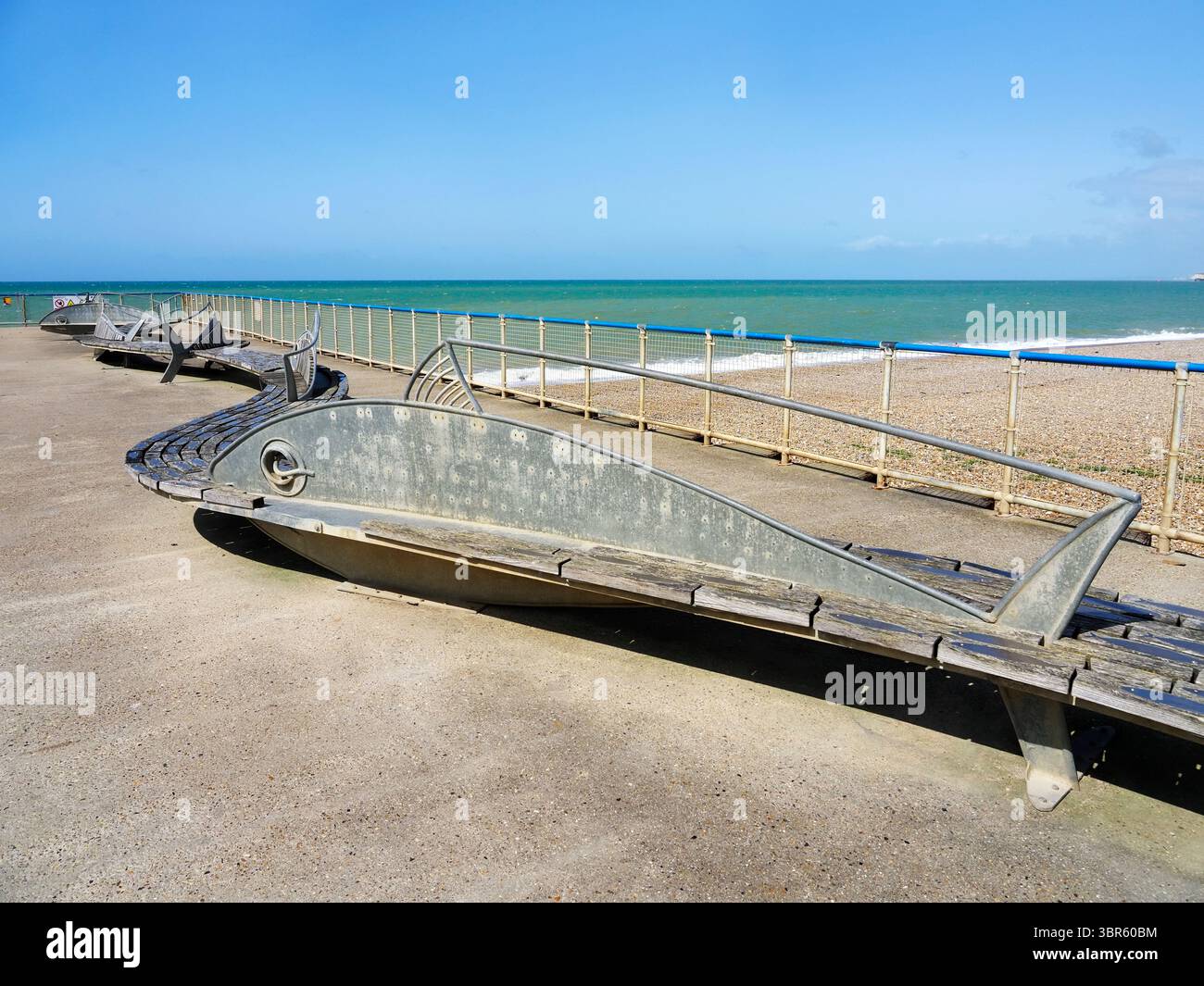 Panchina curva in legno con sculture di pesci sulla frangiflutti di Seaford East Sussex, Inghilterra Foto Stock