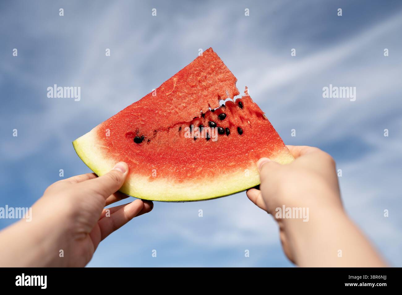 Tenendo una fetta di anguria con i semi contro il cielo. Foto Stock
