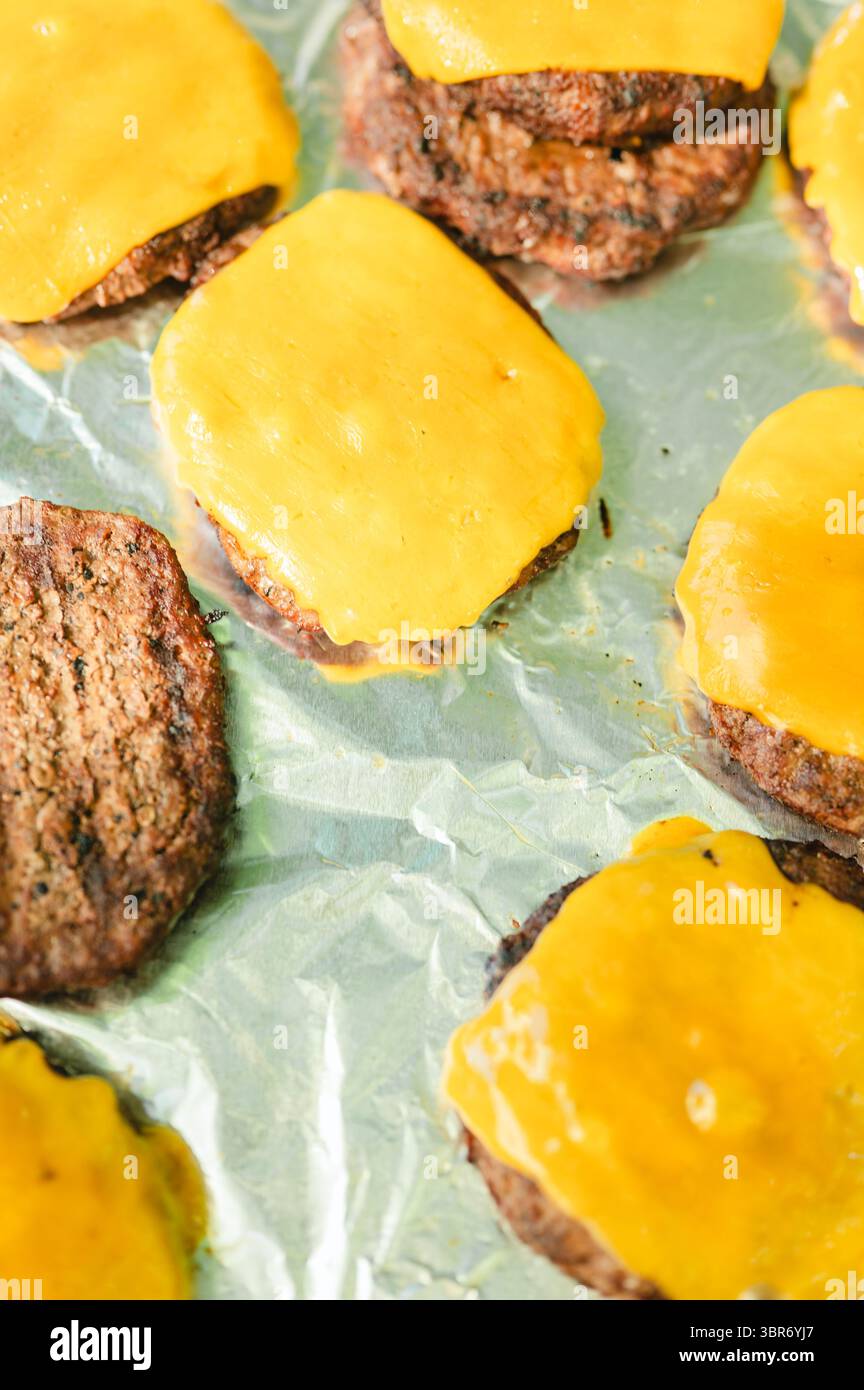 Vista dall'alto dei cheeseburger con formaggio fuso sulla superficie del foglio di alluminio Foto Stock