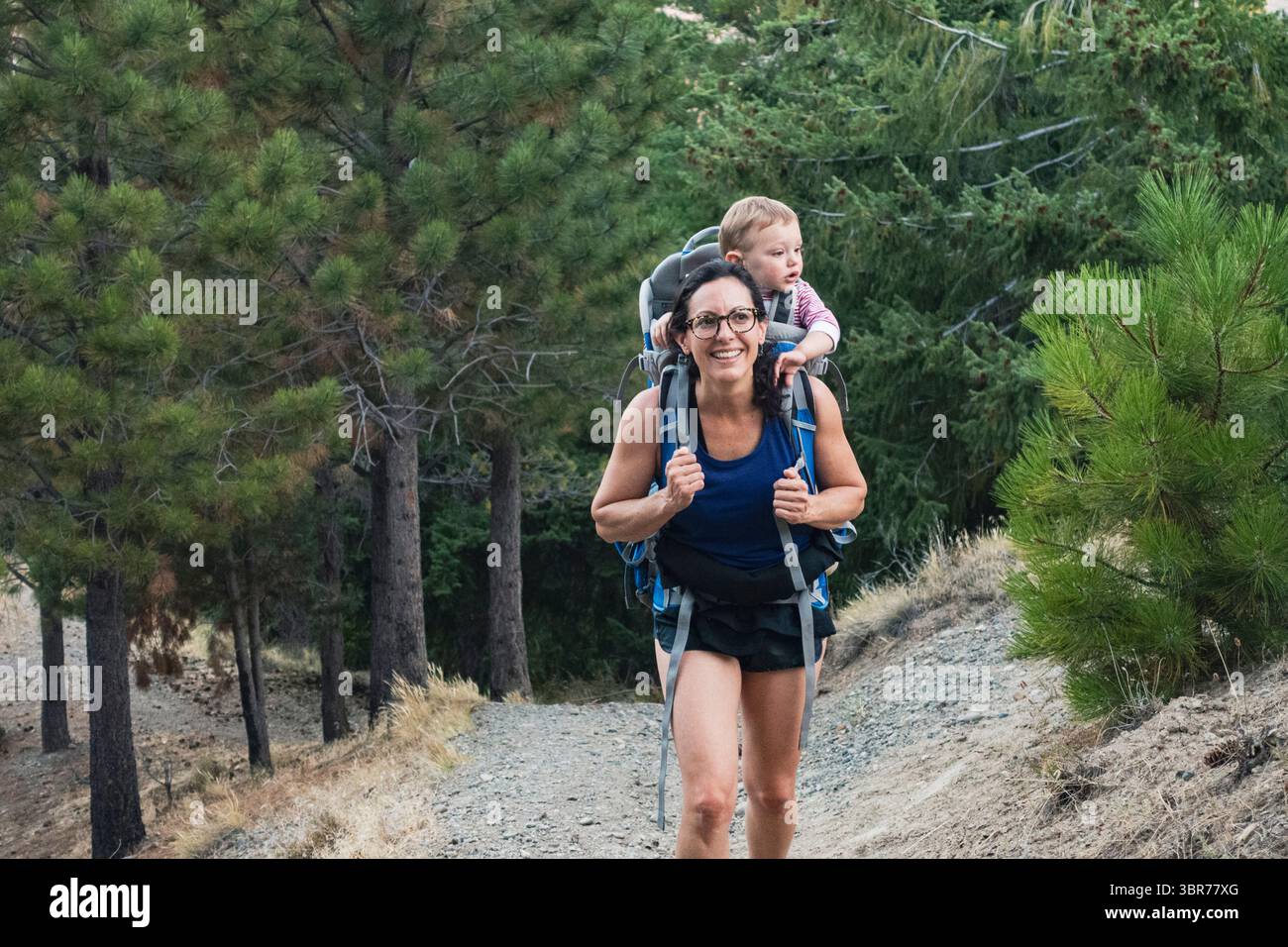 Mamma cammina su un sentiero fuori città portando il suo bambino su uno zaino Foto Stock