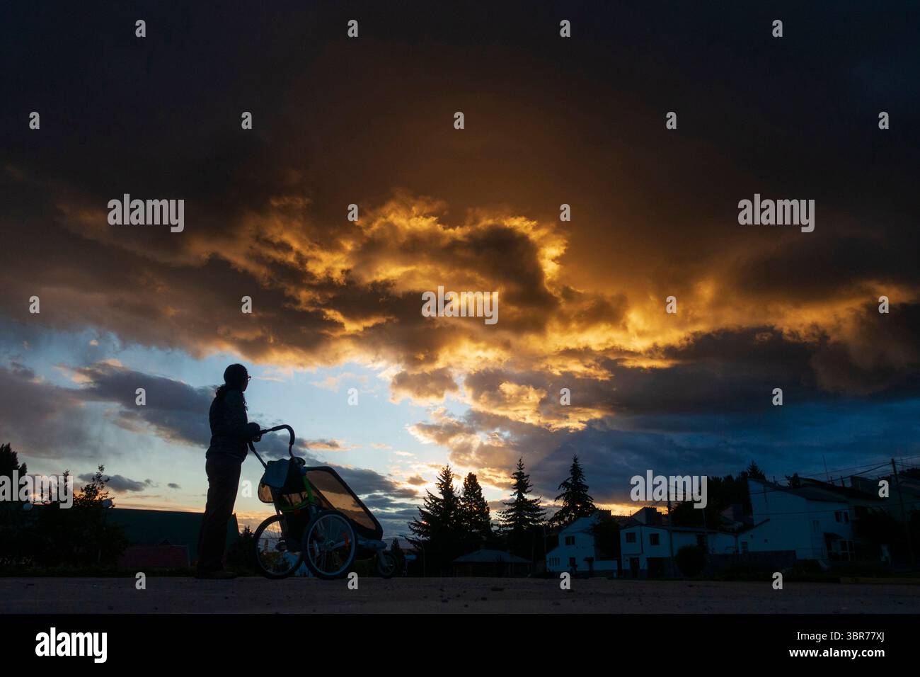 Una madre che fa una passeggiata con un passeggino al tramonto in una piccola città Foto Stock Una madre che fa una passeggiata con un passeggino al tramonto in una piccola città Foto Stock