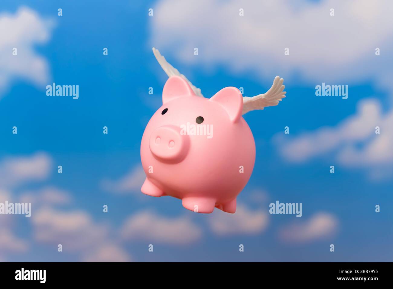 Un salvadanaio con piccole ali bianche che volano contro un cielo blu. Simboleggia concetti relativi al denaro che vola via, alla libertà finanziaria. Foto Stock