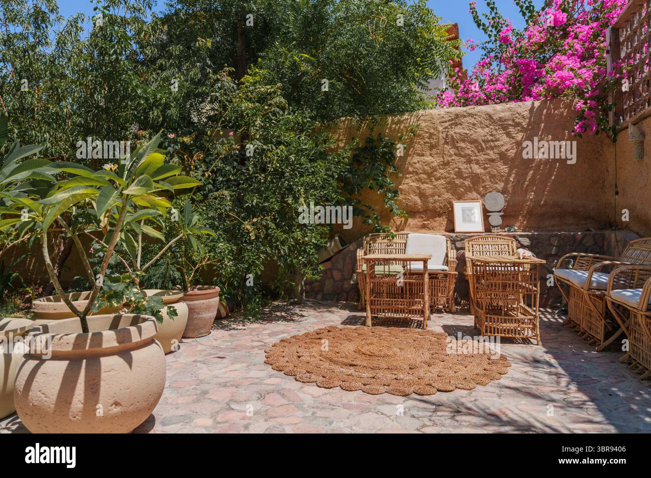 Patio all'aperto boemo con mobili in vimini e bouganville nel soleggiato cortile Foto Stock
