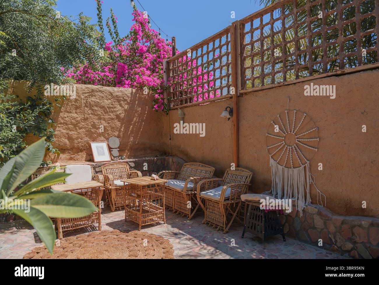 Patio all'aperto boemo con mobili in vimini e bouganville nel soleggiato cortile Foto Stock