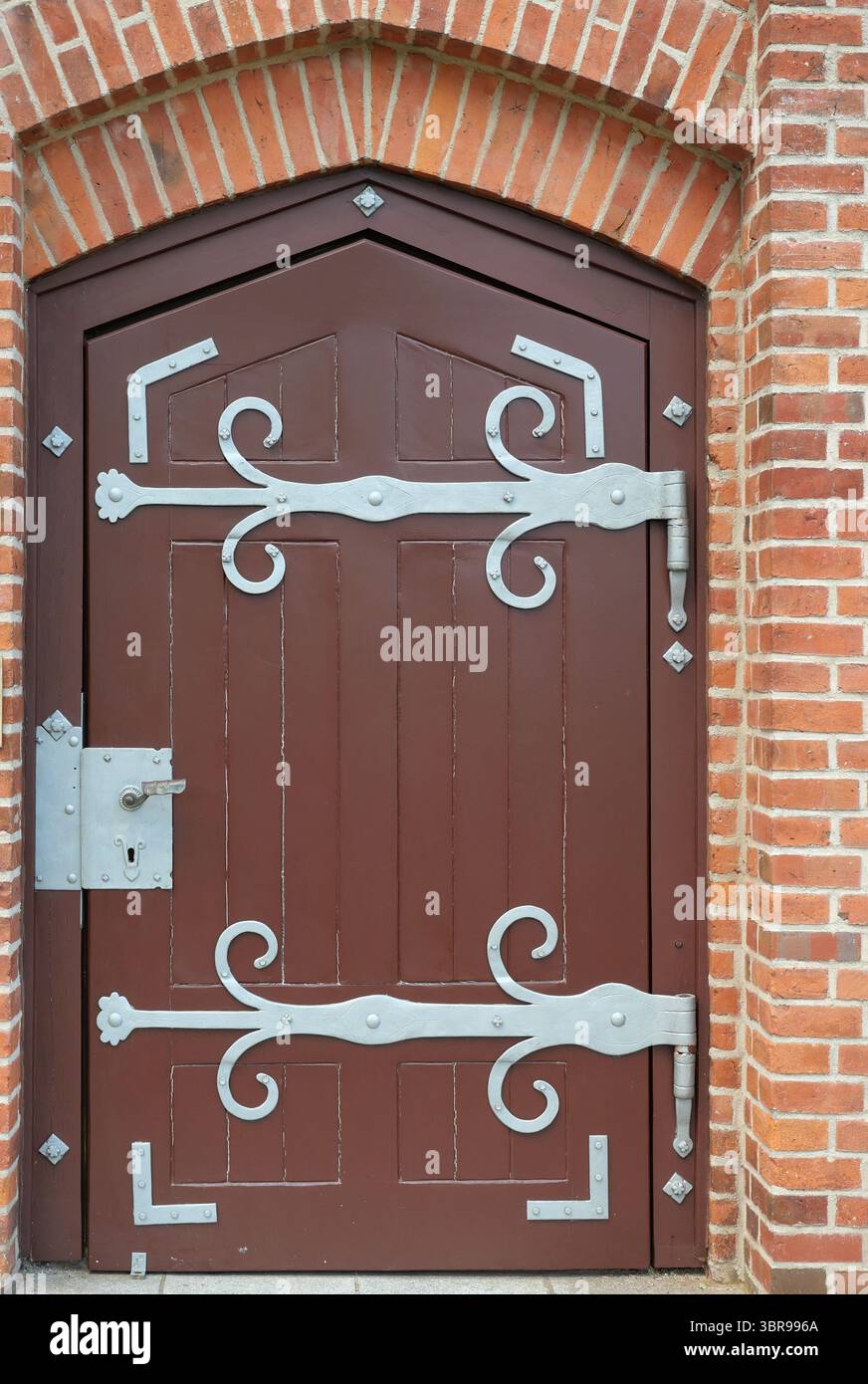 Vecchia porta in legno con cerniere decorative ad arco in mattoni. Ingresso storico dal fascino artigianale. Copyspace Foto Stock