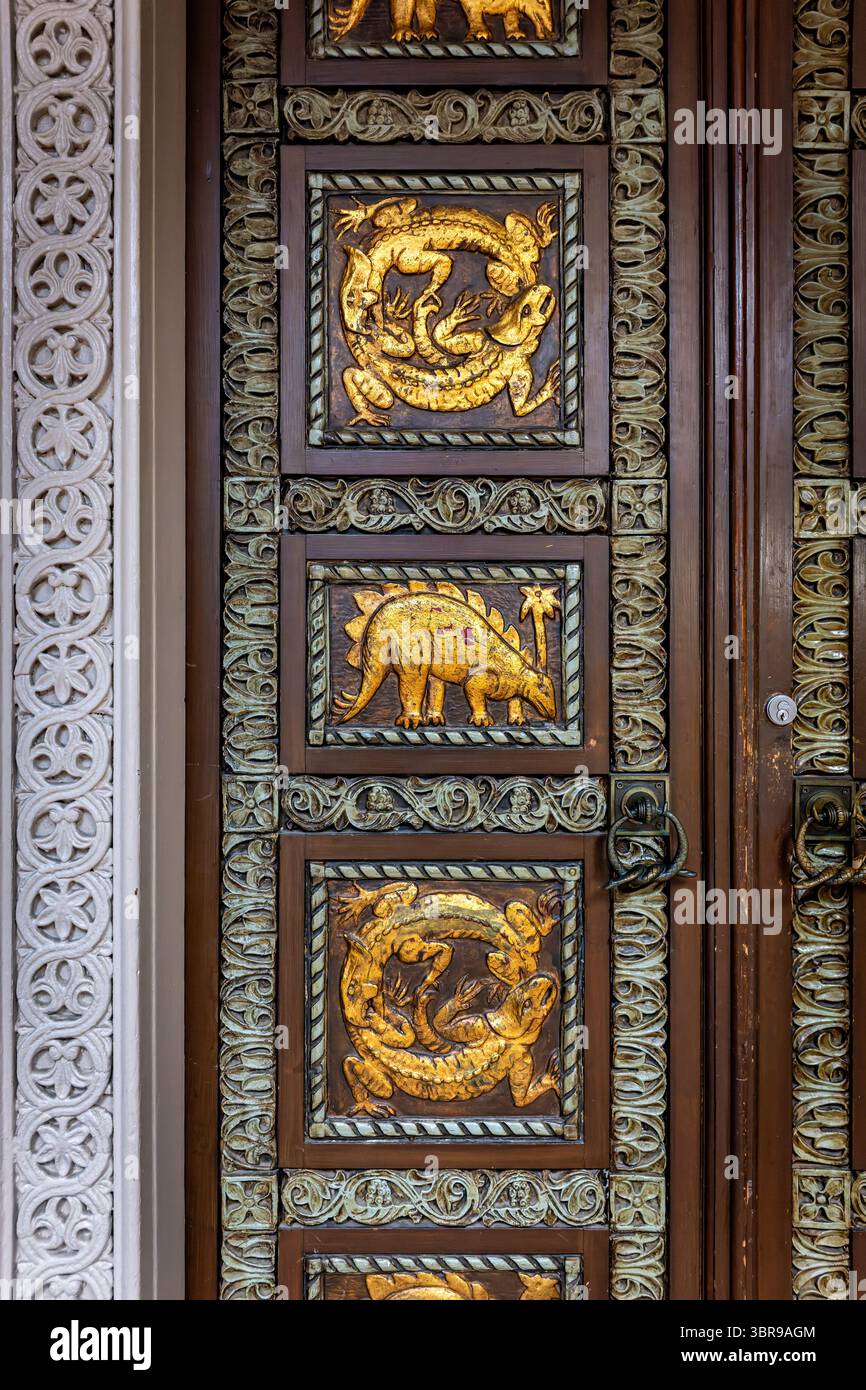 WASHINGTON DC - le porte d'ingresso ornate in legno del Reptile Discovery Center presentano sculture in rilievo d'oro di stegosauro e altri rettili, con maniglie delle porte modellate come serpenti intrecciati. Le porte decorative, risalenti al 1931, facevano parte del progetto completo dell'architetto Albert L. Harris per l'edificio, che includeva il famoso mosaico di stegosaurus creato attraverso la collaborazione con il paleoartista Charles R. Knight e il pioniere del cemento John Joseph Earley. Le porte completano lo stile architettonico bizantino-romanico dell'edificio e riflettono l'approccio dell'era Progressista alla fusione scientifica Foto Stock