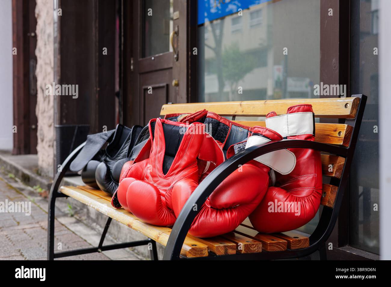 Primo piano di guanti da boxe di colore rosso e nero disposti su una panchina di legno vicino all'ingresso della palestra a lato della strada. Foto Stock