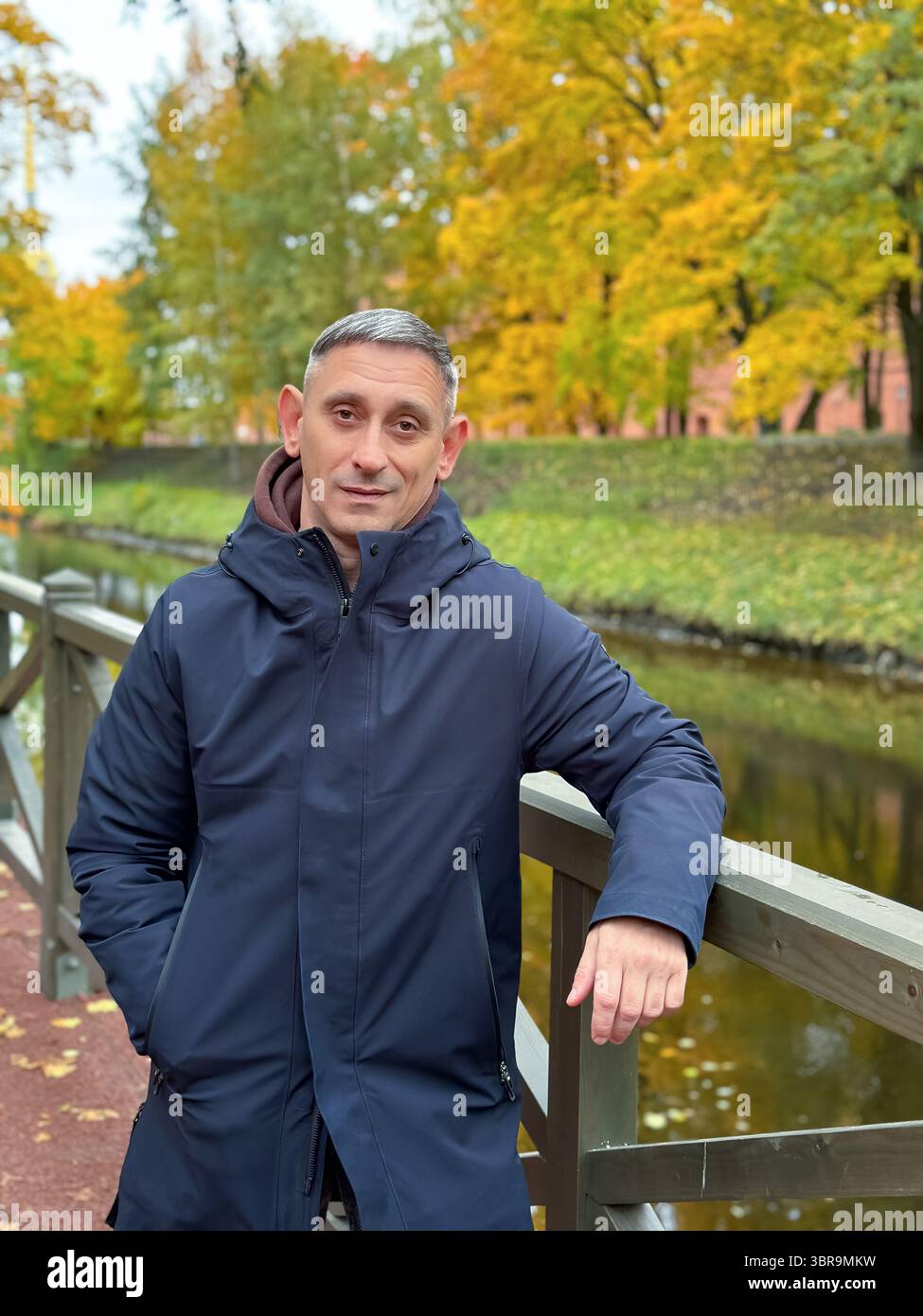 L'uomo con un cappotto nero sta su un ponte. Sta sorridendo. Il ponte è vicino a un fiume Foto Stock