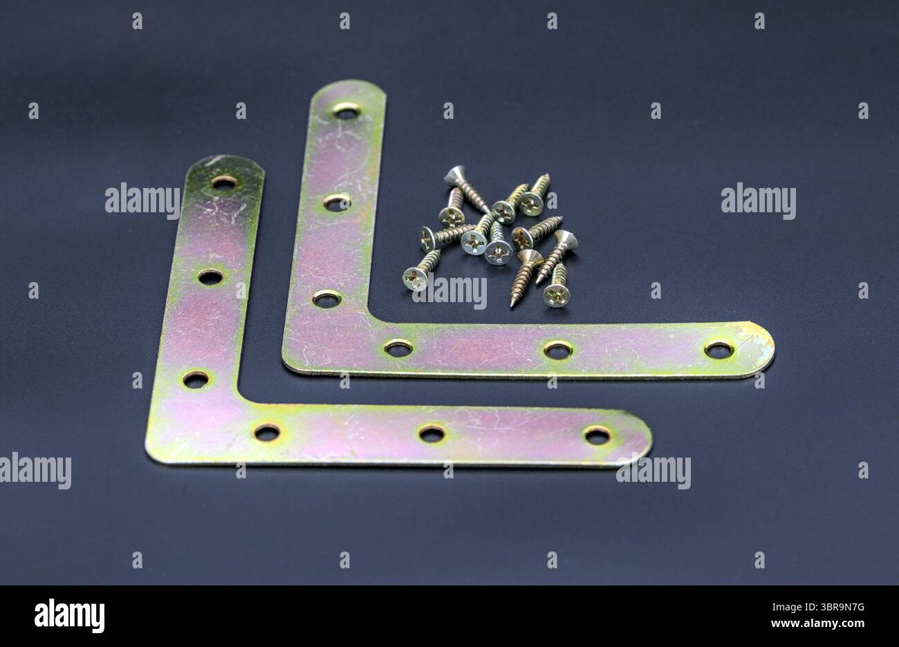 Staffe angolari in metallo con viti su sfondo scuro, che mostrano utensili hardware per la costruzione o progetti fai-da-te. le staffe hanno fori multipli Foto Stock