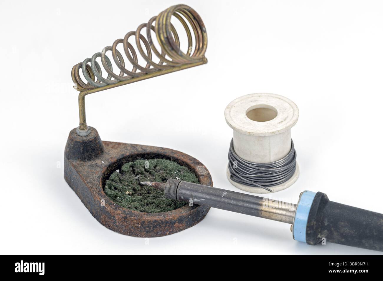 Un saldatore poggia su un supporto accanto alla bobina di filo, mostrando gli strumenti essenziali per il lavoro elettronico. la configurazione è ideale per le attività di saldatura Foto Stock