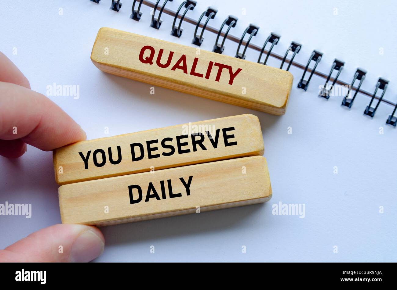 La qualità che meriti ogni giorno testo su blocchi di legno e blocco note rafforza la coerenza come abitudine quotidiana di eccellenza. Foto Stock