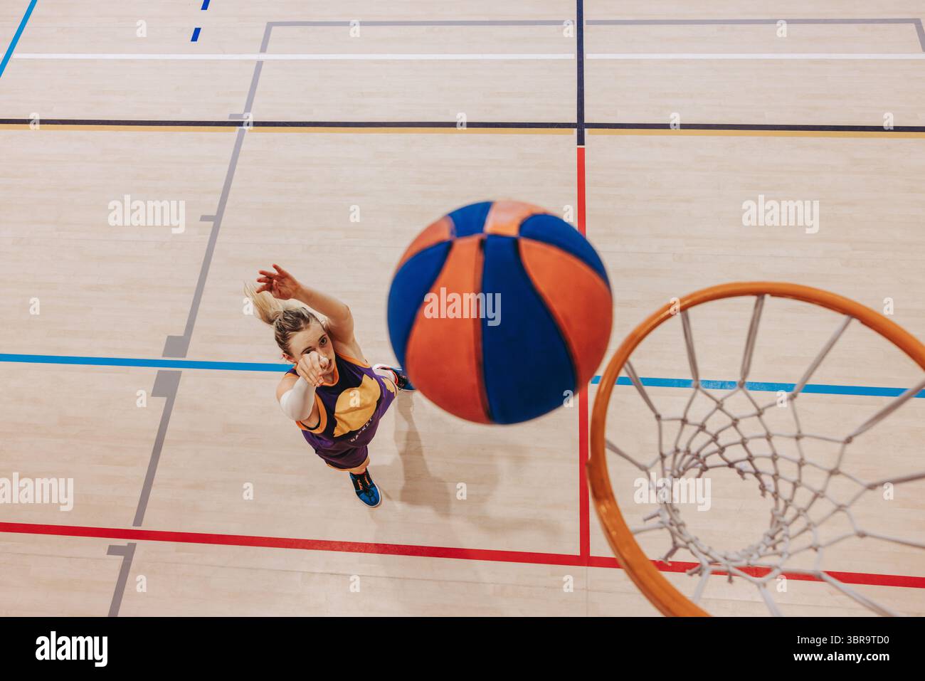 Una giovane giocatrice di basket in azione, che mira e tira con abilità la palla verso il cerchio durante una partita al chiuso, mostrando precisione e Foto Stock