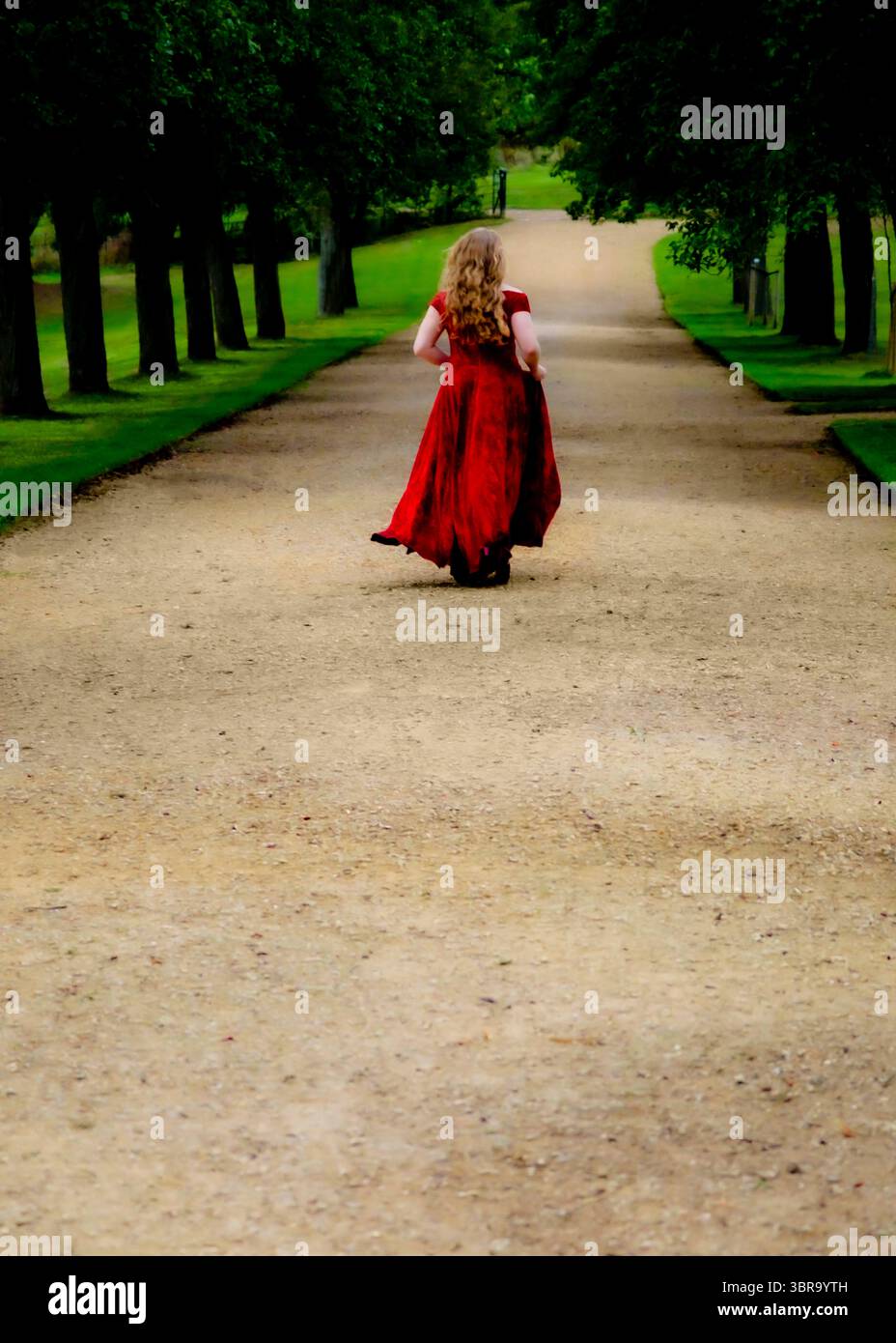 Una donna con un vestito rosso corre lungo un sentiero fiancheggiato da alberi. Foto Stock