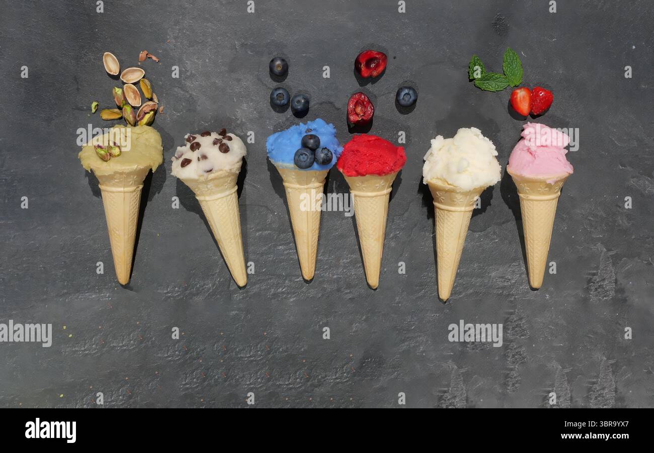 Coni assortiti di waffle fatti in casa di gelato in fila, dal sapore diverso colorato su sfondo ardesia Foto Stock