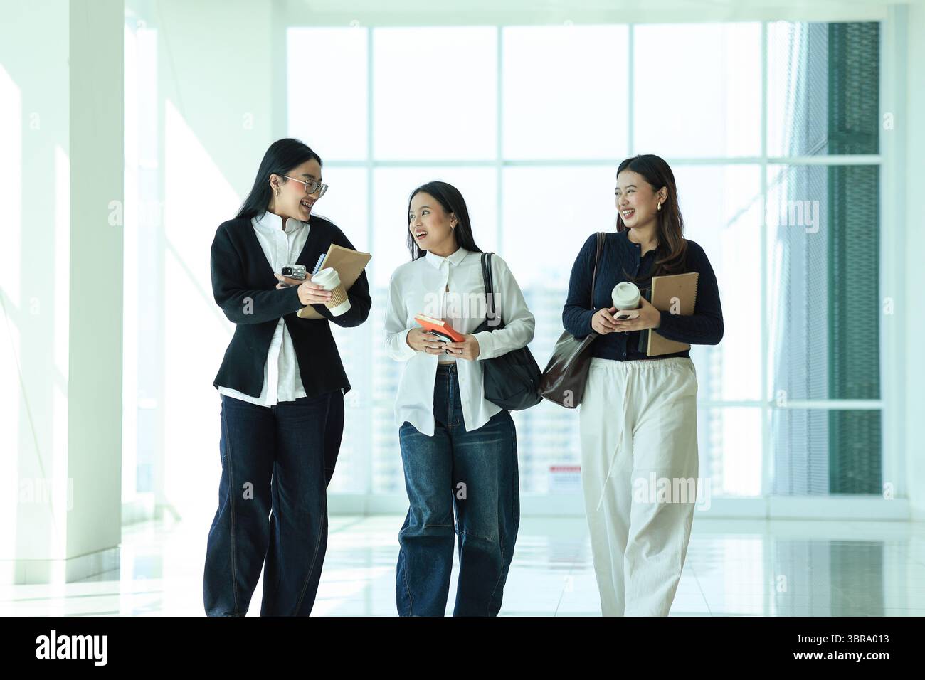 Happy Three Asian College Student Classmate che cammina sul corridoio Campuss mentre chiacchiera e discuti Foto Stock