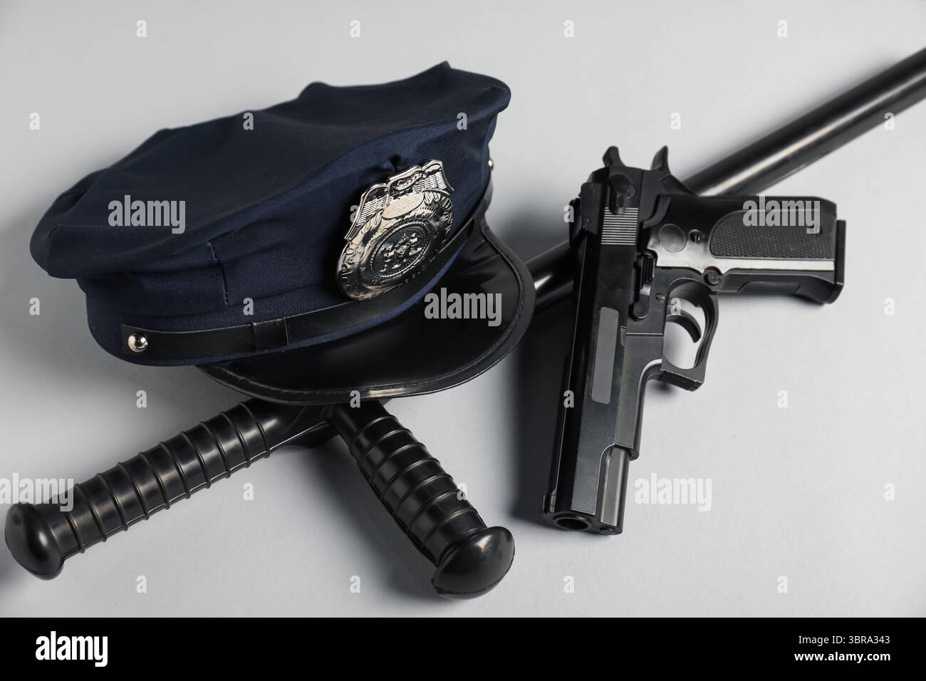 Cappellino della polizia, pistola e bastone su sfondo bianco, primo piano Foto Stock