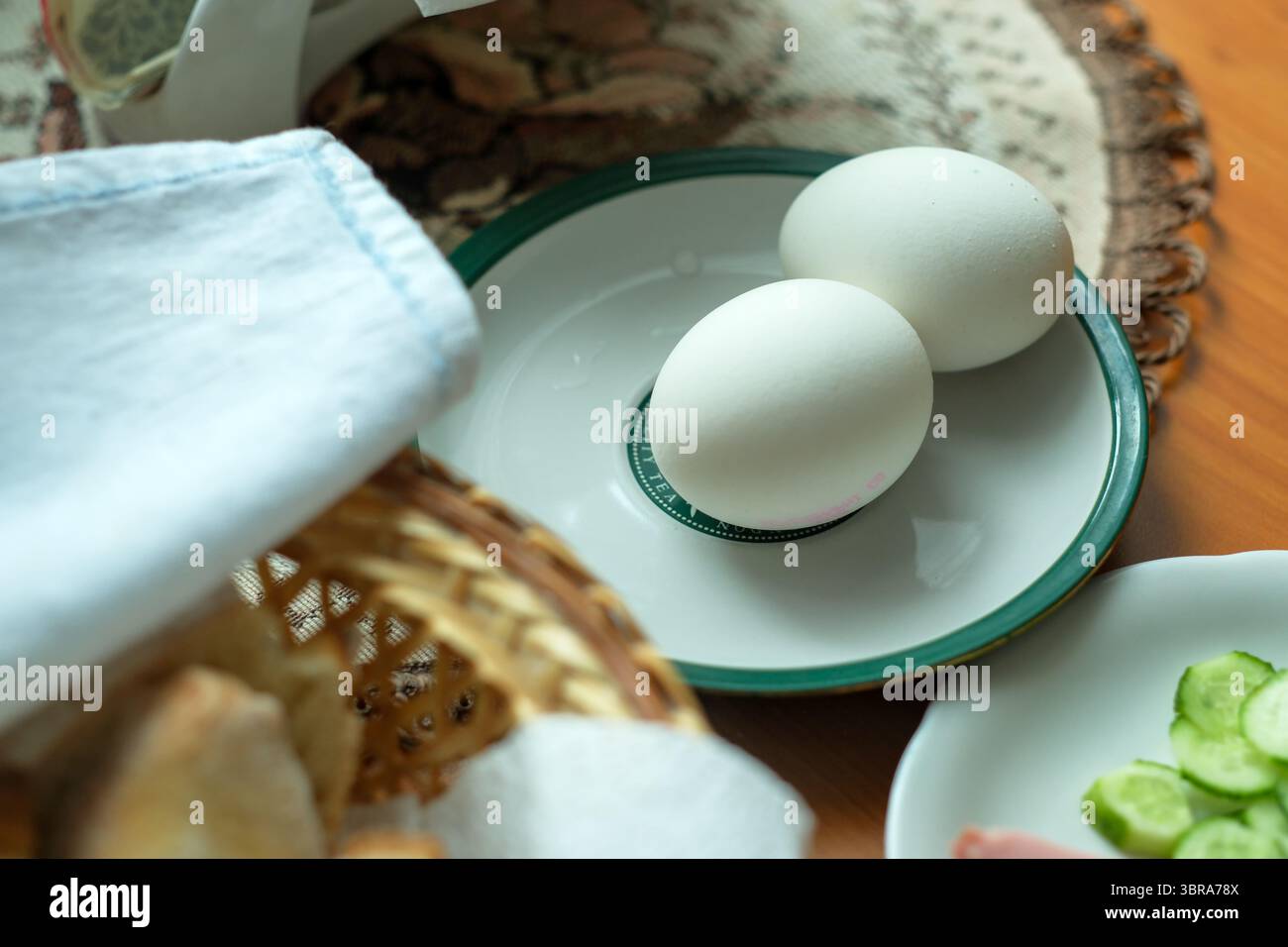Due uova bianche poggiano su un piatto con bordi verdi accanto alle verdure fresche. Foto Stock