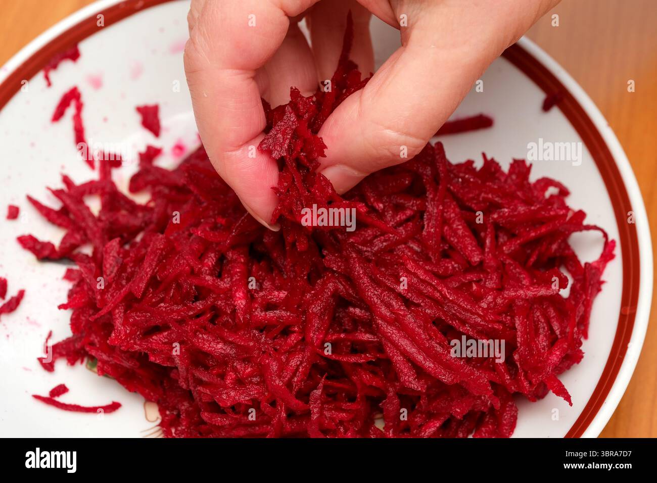 Le mani triturano sapientemente barbabietole rosse su un piatto bianco tradizionale, pieno di sapore. Foto Stock