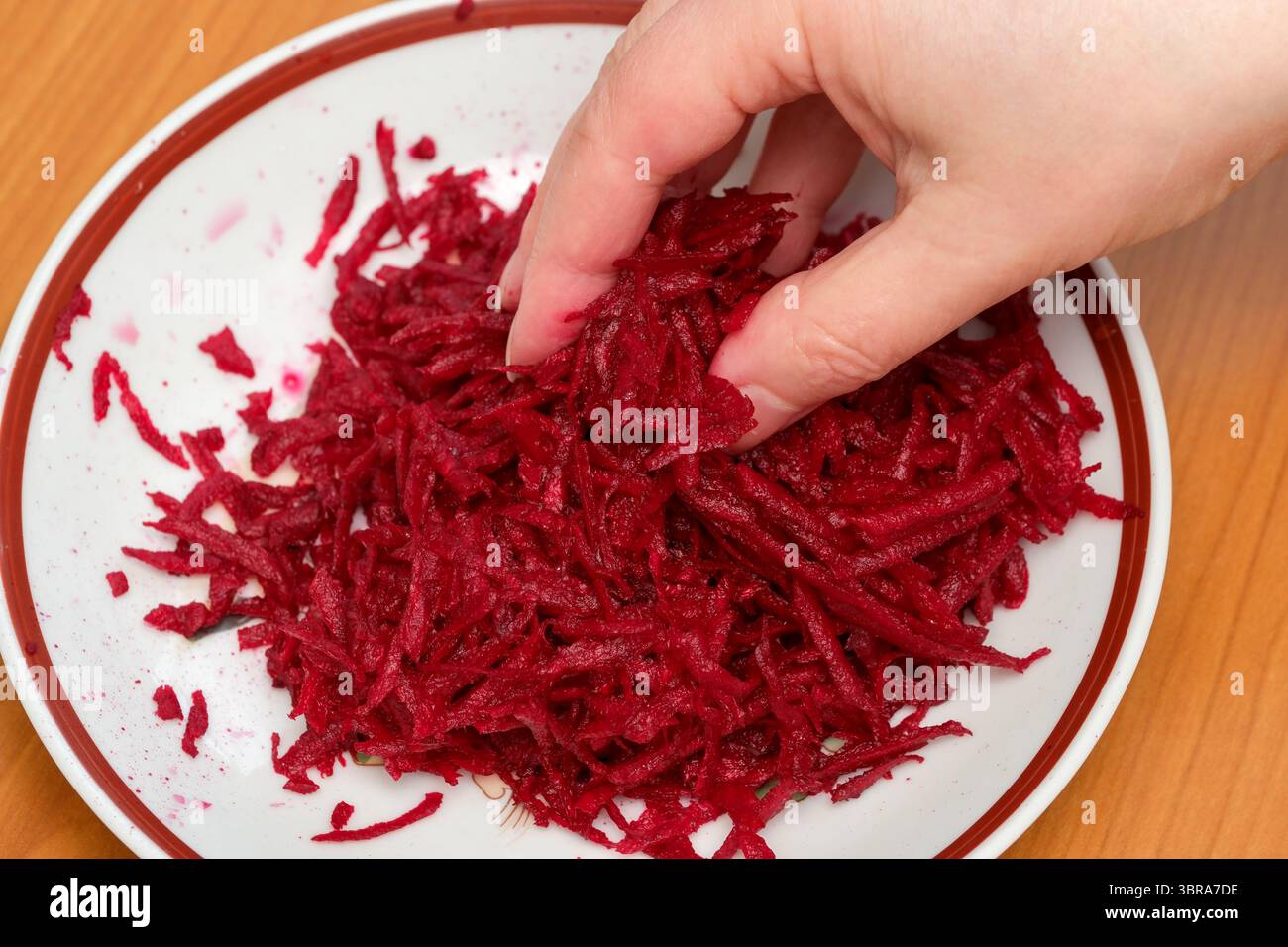 Una mano raccoglie delicatamente la barbabietola grattugiata, pronta a creare un'insalata vivace. Foto Stock