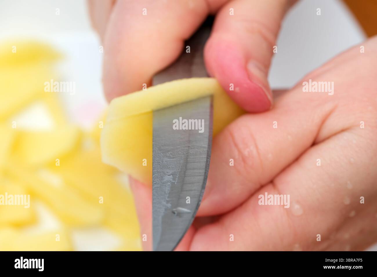 Le dita guidano abilmente un coltello per sbucciare una patata, mostrando precisione culinaria e calore. Foto Stock