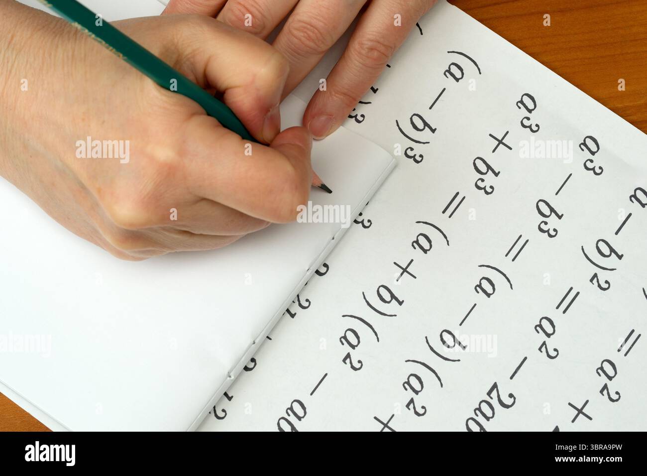 Le mani risolvono con attenzione le equazioni matematiche su un blocco note su una scrivania di legno. Foto Stock