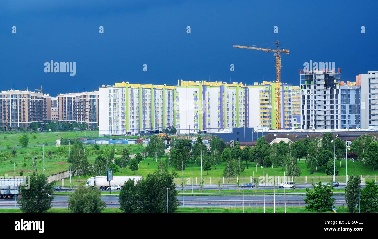 Le nuvole scure sorvolano una città in crescita, contrastando la costruzione con il verde. Foto Stock
