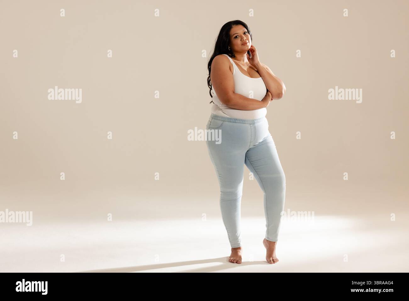 Modello femminile che posa a piedi nudi in studio con canotta bianca e jeans leggeri, spazio fotocopie Foto Stock