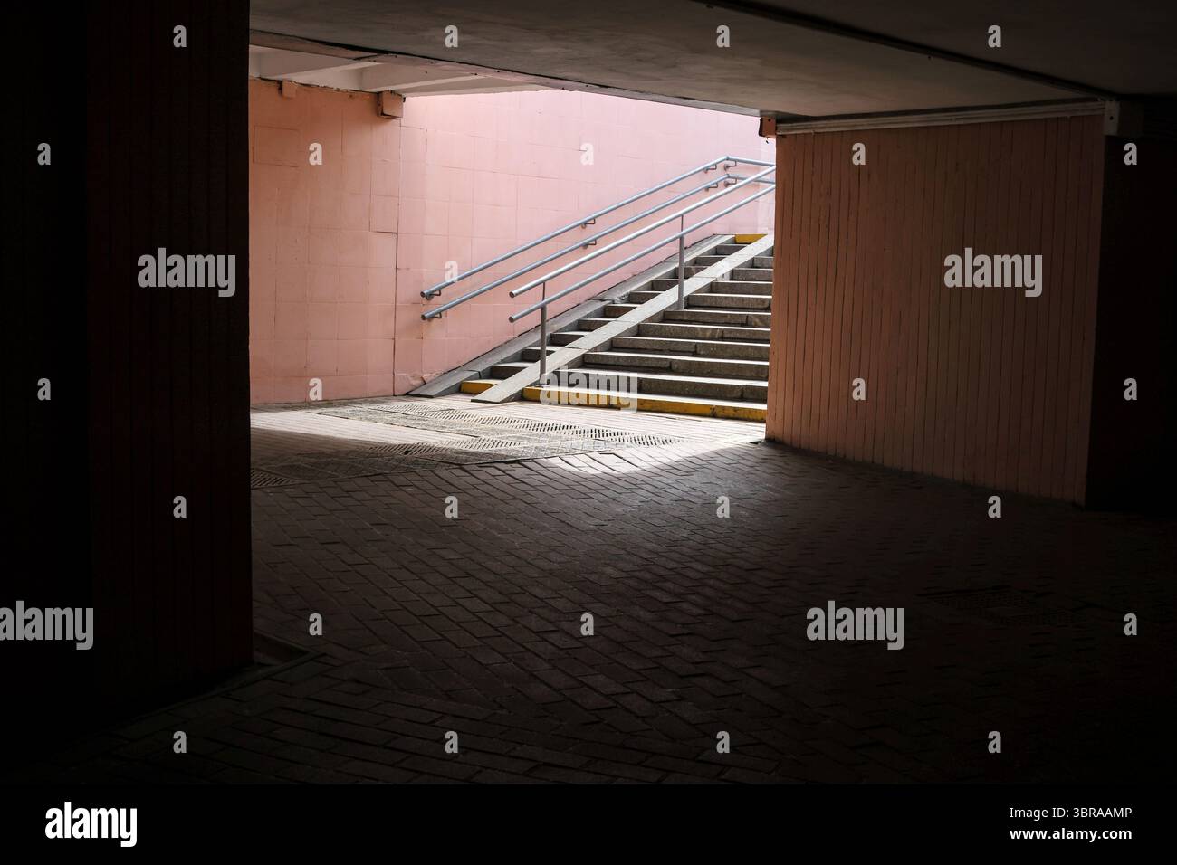 Un corridoio poco illuminato si apre su una scala che porta alla vibrante luce del giorno all'esterno. Foto Stock