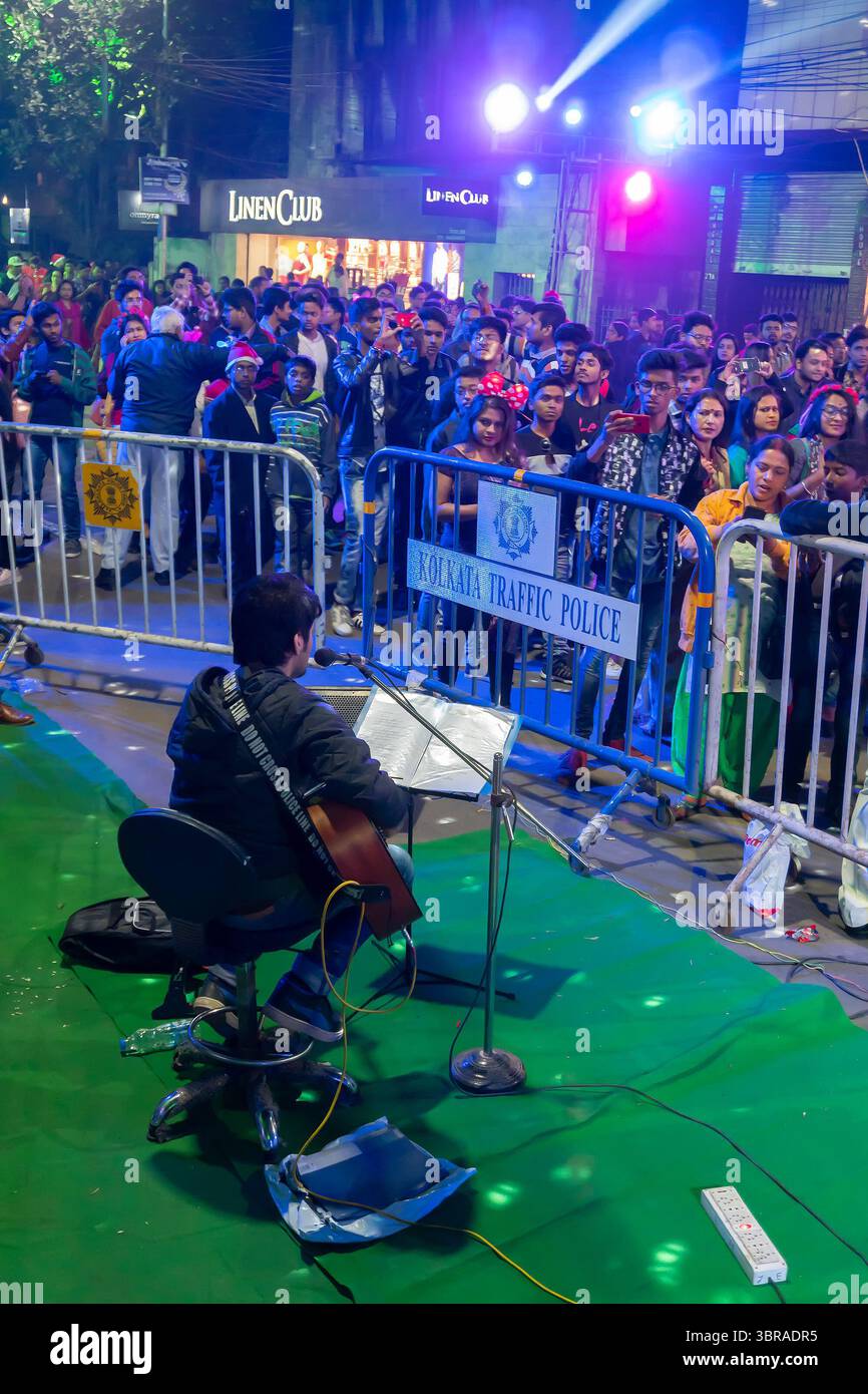 Kolkata, Bengala Occidentale, India - 25.12.2018 : cantante di strada che canta canzoni natalizie mentre i giovani si divertono a Park Street illuminata. Foto Stock