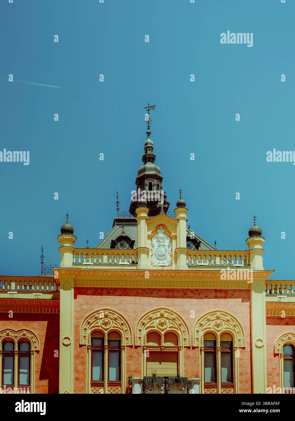 Storico edificio ornato con finestre decorative e guglie sotto il cielo azzurro a Novi Sad, Serbia Foto Stock