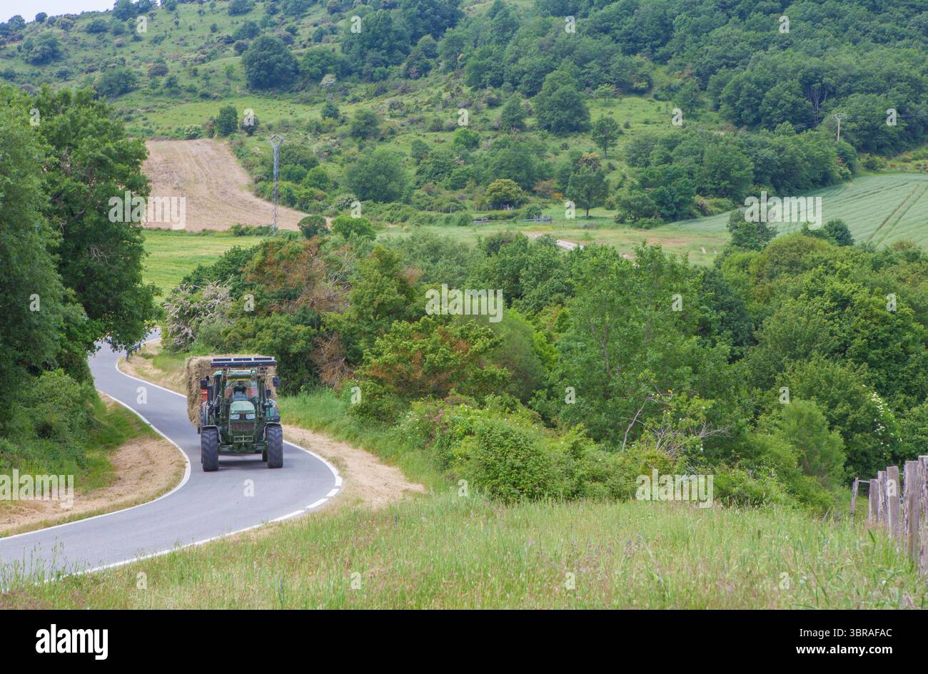 Trattore che tira il rimorchio della paglia attraverso la strada montuosa locale. L'agricoltura di montagna Foto Stock