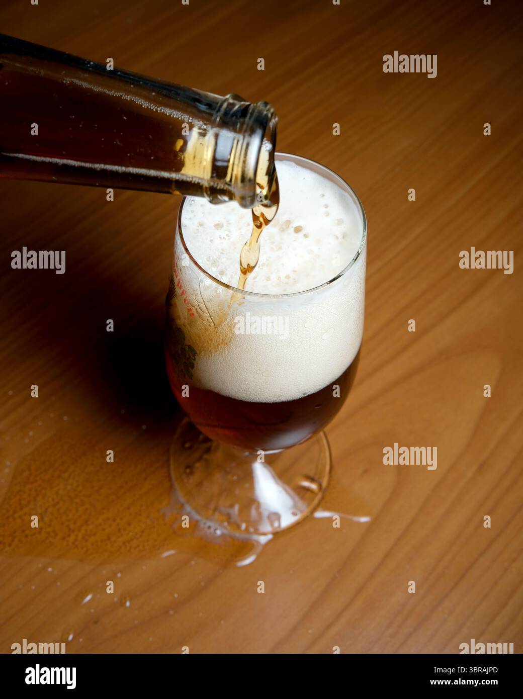 Il liquido ambrato riempie il bicchiere, creando bolle di schiuma quando fuoriesce. Foto Stock