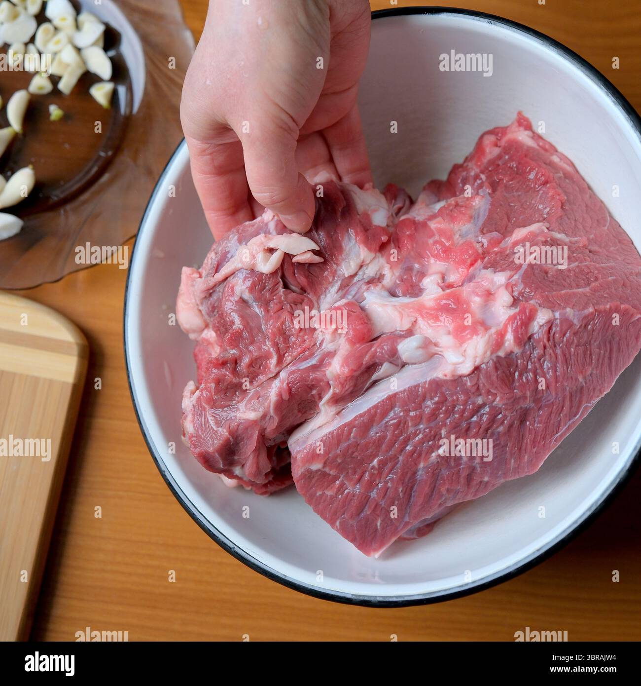 La mano posiziona un pezzo di carne cruda in un recipiente, pronto per la cottura. Foto Stock