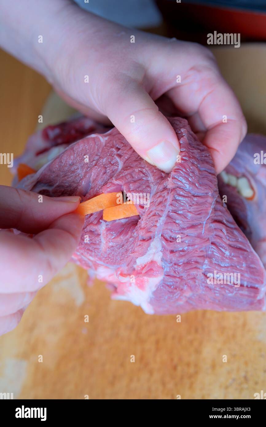 Le mani inseriscono sapientemente le carote nella carne tenera, dimostrando la loro competenza culinaria. Foto Stock