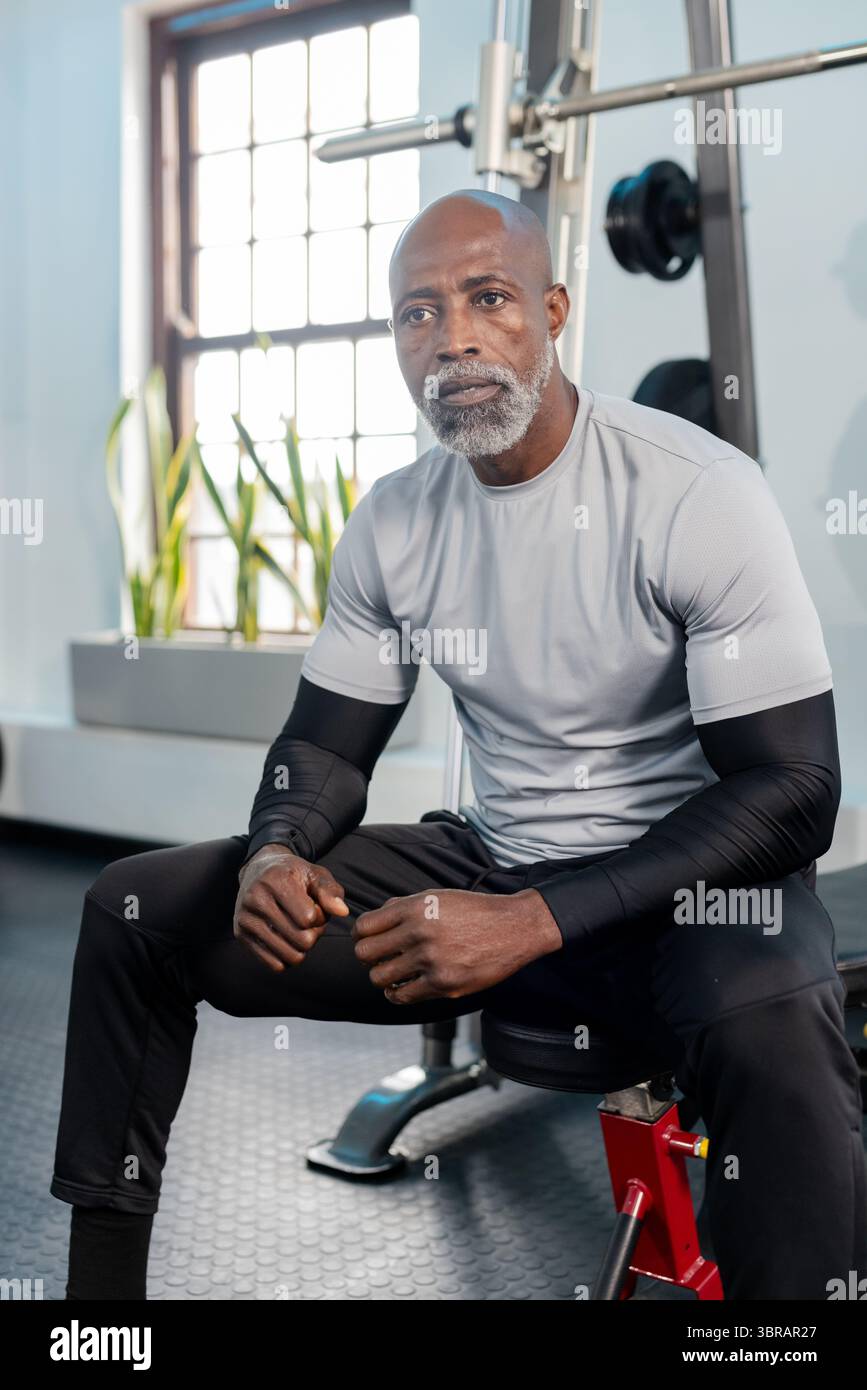 Uomo afro-americano seduto su una panchina di pressa in palestra afferrando il campanile con piastre per pesi Foto Stock