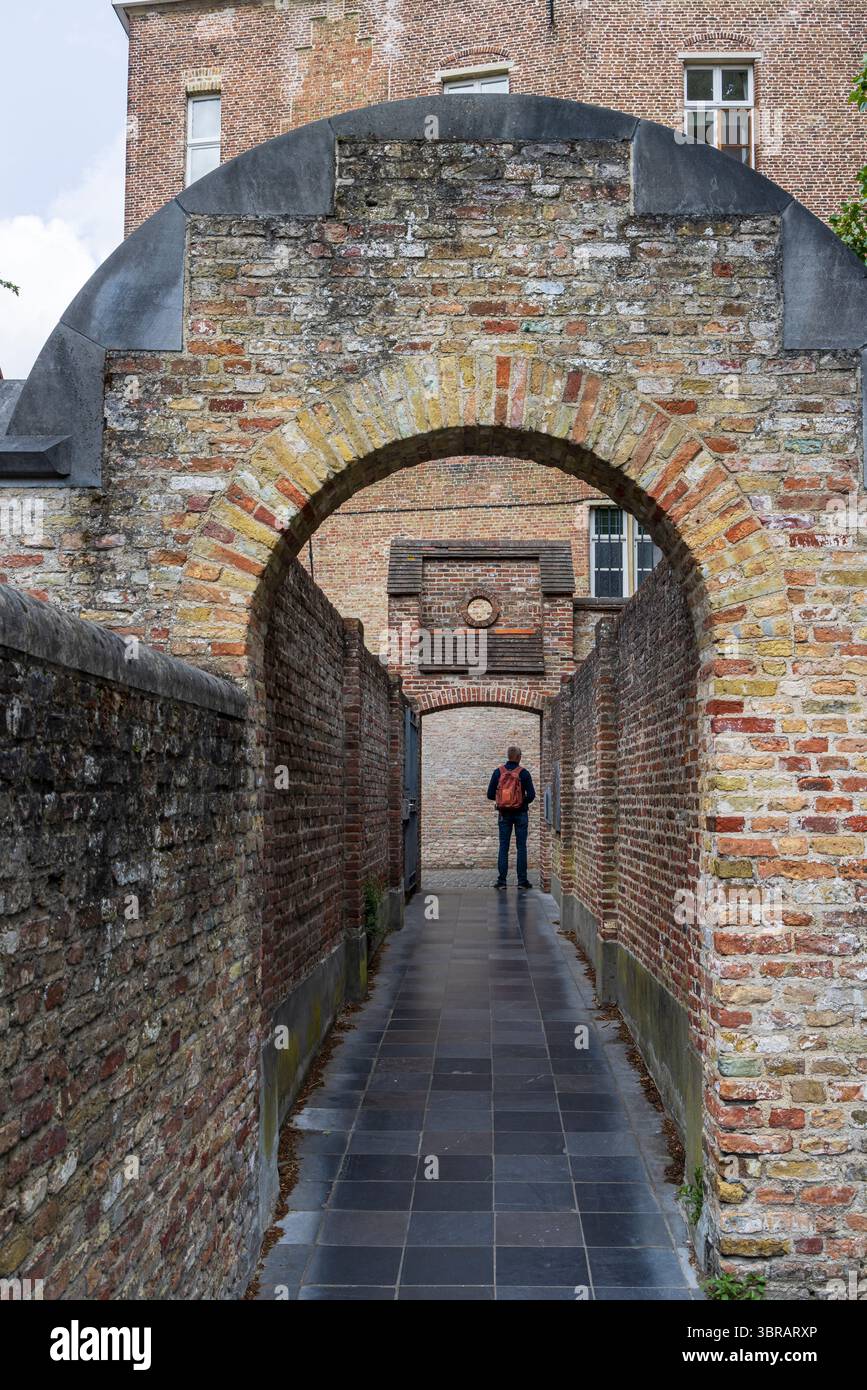Turista che passa davanti a un antico vicolo con arco d'ingresso a Bruges, in Belgio Foto Stock