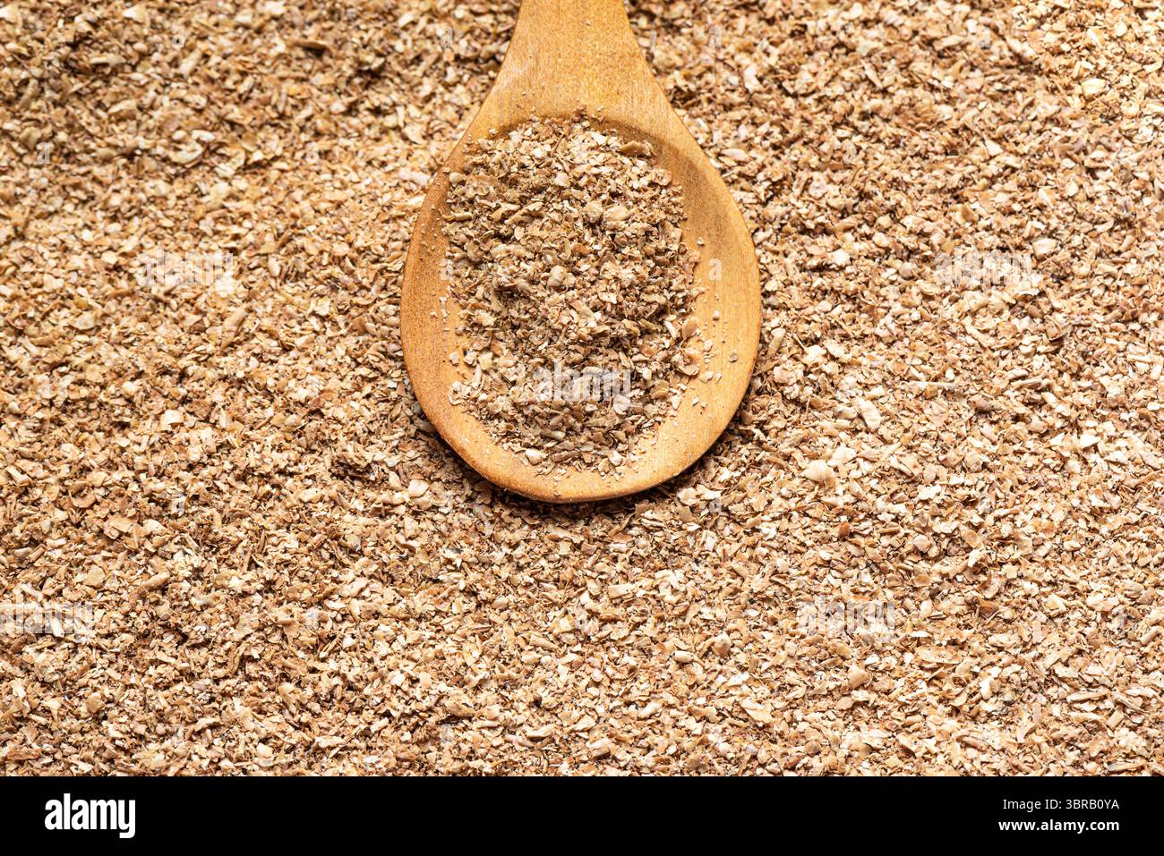 Fibra di crusca di grano su cucchiaio di legno, primo piano. Consistenza dettagliata di vari prodotti di crusca istantanea di cereali. Mangiare sano. Foto Stock