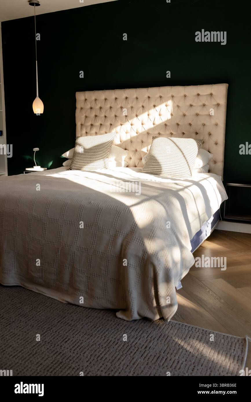 La camera da letto principale presenta testiera trapuntata con piumone trapuntato accanto alla lampada e alla lampada a sospensione Foto Stock