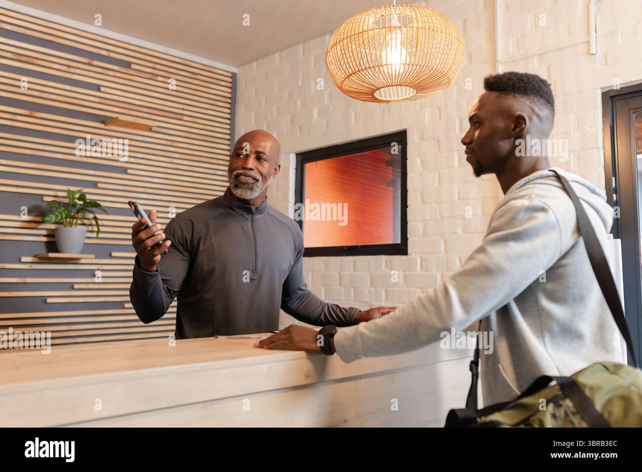 Uomini afroamericani che discutono di fitness al banco della reception tenendo in mano smartphone e borsone Foto Stock
